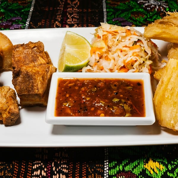 Fried pork belly, yuca fries, coleslaw, lime, and dipping sauce on a white plate.