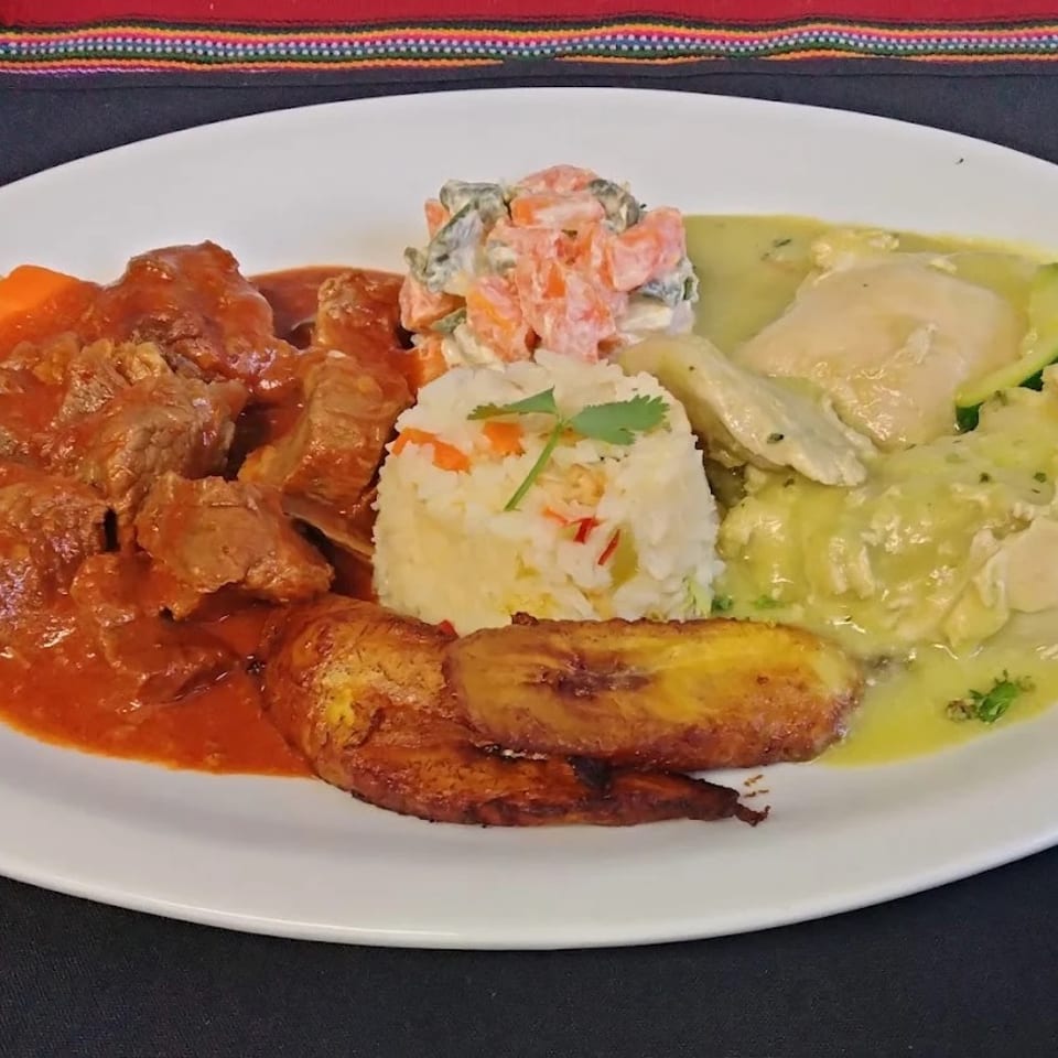 Platter featuring red-sauced meat, creamy green chicken, seasoned rice, fried plantains, and vegetable salad.