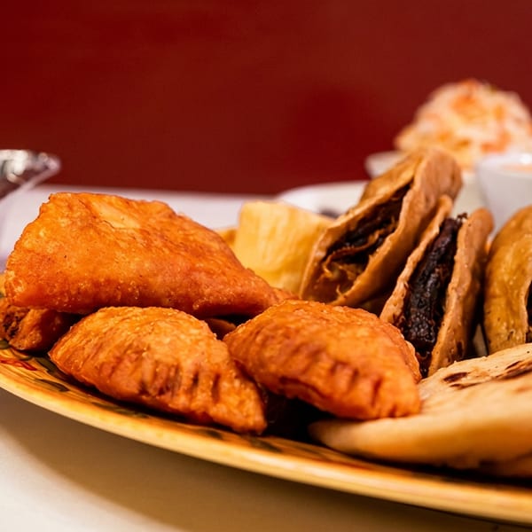 A platter of golden-fried empanadas, mini tacos, and flatbreads, with sides in the background.